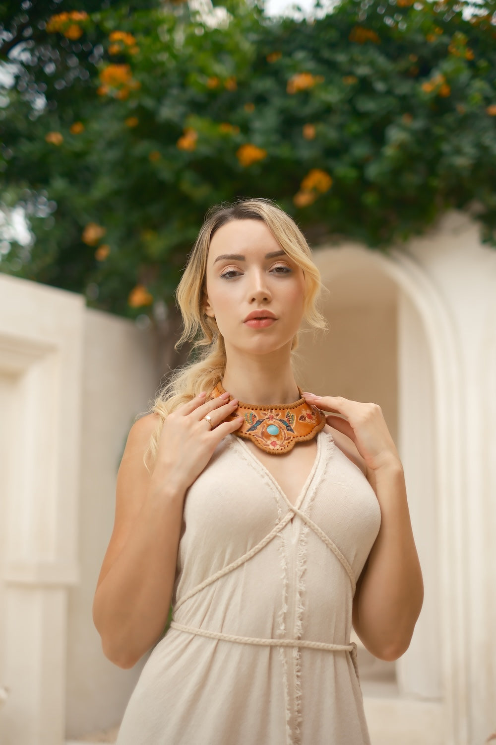 Close-up of artisan leather choker featuring turquoise gemstone and hand-painted floral and bird motifs in earthy tones, adjustable fit.