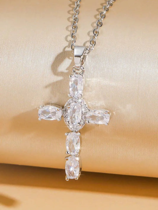 Silver cross-shaped pendant necklace with clear stones on a beige fabric background
