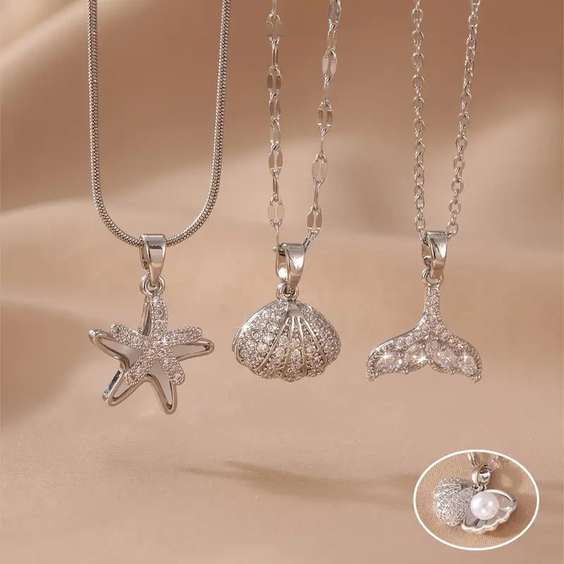 Three silver pendants shaped like a starfish, shell, and tail on a beige background